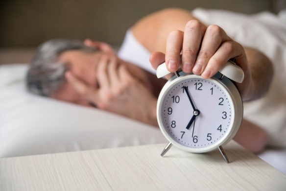 Man lying in bed turning off an alarm clock in the morning at 7a